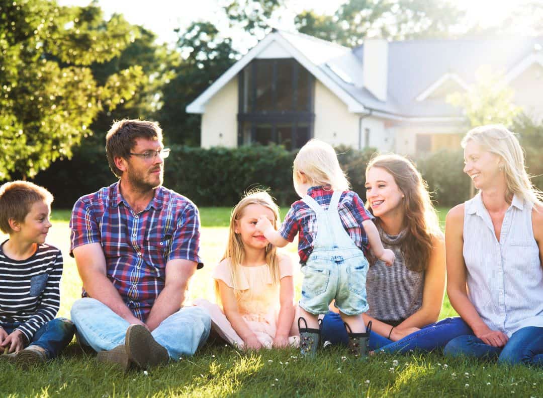 Family sitting together on a green lawn in front of a house.