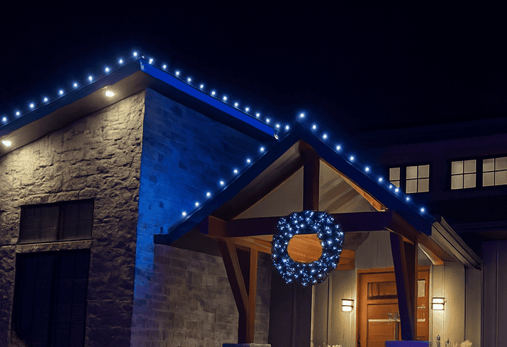 How to Remove Outdoor Christmas Lights After the Holidays Stone home at night with blue C9 lights along the roofline and a covered front entry with a lit wreath